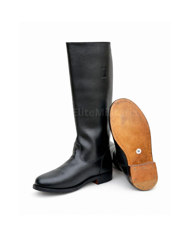 May include: A pair of black leather riding boots. One boot is upright, the other is lying on its side, revealing the sole. The soles are a light brown color, and the boots have a classic design.