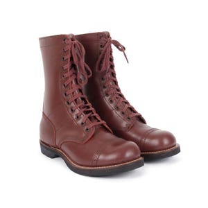 Puede incluir: Un par de botas de cuero burdeos con cordones. Las botas tienen puntera y suela resistente. Los cordones y las costuras son de color burdeos a juego. Un estilo de bota clásico.