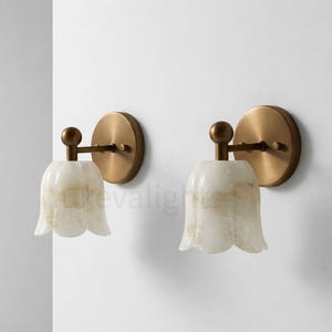 May include: Two wall sconces with a tulip-shaped, off-white shade and a brass-colored metal base. The sconces are mounted on a white wall. The shades have a marbled appearance.