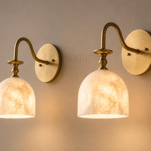 Pair of modern alabaster wall sconces with antique brass finish, handcrafted mid century bathroom vanity wall lights on a warm beige textured wall
Pair of handcrafted alabaster brass wall lights, modern mid century wall sconces for bathroom, bedroom, or entryway
Modern brass wall sconce pair with natural alabaster shades, elegant luxury bathroom vanity lighting fixture
Antique brass alabaster wall light fixture, handmade modern wall sconces with warm illumination for luxury interiors