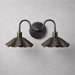May include: A double wall sconce light fixture featuring a circular backplate and two curved arms extending to support two downward-facing, fluted, bell-shaped shades. The entire fixture is finished in a dark, weathered bronze metal tone.