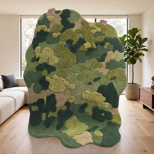 May include: A large, abstract rug with a camouflage pattern in shades of green, beige, and brown. The rug has a unique, organic shape and a textured surface, adding visual interest to the room. The rug is held up by unseen hands.