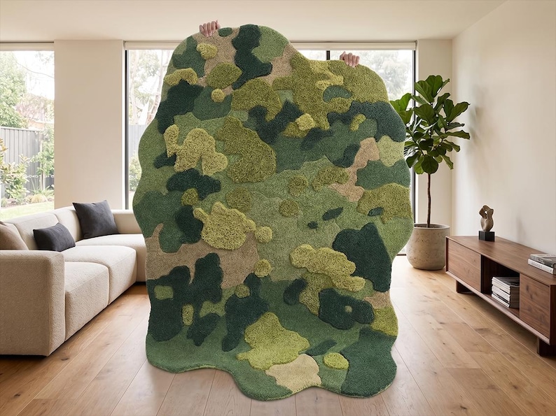 May include: A large, abstract rug with a camouflage pattern in shades of green, beige, and brown. The rug has a unique, organic shape and a textured surface, adding visual interest to the room. The rug is held up by unseen hands.