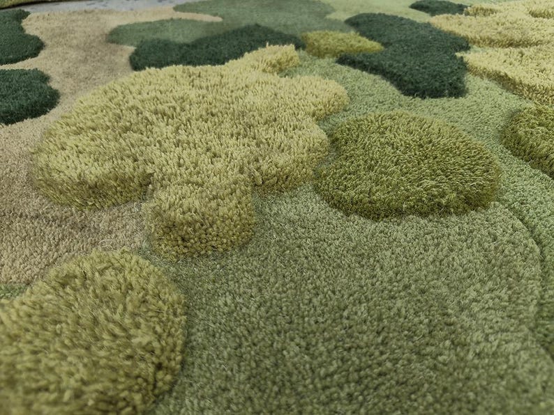May include: A close-up view of a green and tan rug with a textured, tufted design. The rug features various shades of green and tan, with raised, cloud-like shapes. The design creates a soft, plush appearance, suitable for home decor.