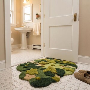 May include: A unique, organic-shaped rug with a mossy, textured appearance. The rug features shades of green, tan, and brown, resembling a landscape. Two brown slippers are placed near the rug on a white tile floor.