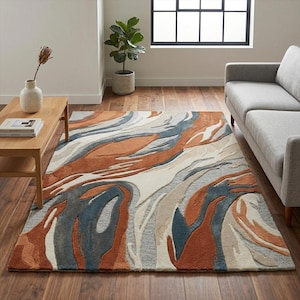 Op de afbeelding: Een rechthoekig vloerkleed met een abstract ontwerp in roest, blauw, grijs en crème. Het vloerkleed heeft een wervelend patroon, waardoor een textuur ontstaat. Het ligt op een houten vloer en vormt een aanvulling op het interieur.
