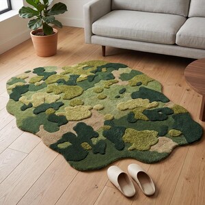 May include: A camouflage-patterned rug in shades of green, beige, and brown, with an irregular, organic shape. The rug is placed on a hardwood floor, with a sofa, coffee table, and plant visible in the background. A pair of cream-colored slippers are on the floor.