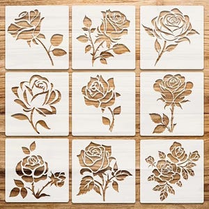Peut inclure: Neuf pochoirs carrés avec des motifs de roses. Chaque pochoir a un fond blanc avec un motif de rose en bois découpé. Les roses varient en style, certaines montrant des fleurs complètes et d'autres des bourgeons et des tiges.