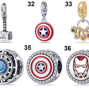 May include: A collection of six silver-toned metal jewelry charms featuring superhero-themed designs, including a hammer, a circular shield, a gold-toned ring with colorful stones, and three round beads with detailed enamel and crystal accents.