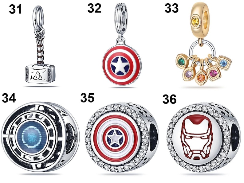 May include: A collection of six silver-toned metal jewelry charms featuring superhero-themed designs, including a hammer, a circular shield, a gold-toned ring with colorful stones, and three round beads with detailed enamel and crystal accents.