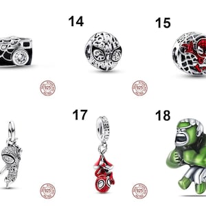 May include: A collection of six sterling silver charms featuring Marvel characters and motifs. Item 13 is a camera, 14 is a spherical charm with text, 15 is a web-patterned sphere with a red figure, 16 and 17 are hanging charms, and 18 is a green figure.