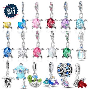 Può includere: Una collezione di ciondoli a forma di tartaruga in argento, ognuno con un guscio di pietra preziosa di colore diverso. I ciondoli sono progettati per essere utilizzati come pendenti o per braccialetti. L'immagine include una promozione "COMPRA 2 PRENDI 1 GRATIS".