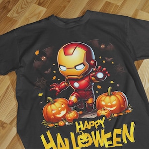 Puede incluir: Una camiseta negra de manga corta con un gráfico de un personaje de Iron Man estilo dibujo animado rodeado de calabazas de Halloween naranjas y murciélagos. El texto "HAPPY HALLOWEEN" está impreso en letras amarillas grandes.