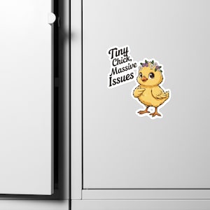 Può includere: Un adesivo con un pulcino dei cartoni animati con una corona floreale. Il pulcino è giallo con zampe e becco marroni. Il testo sull'adesivo recita "Tiny Chick, Massive Issues" in nero. L'adesivo è su una superficie bianca.