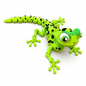 May include: A bright lime green articulated lizard figurine featuring black spots across its body and tail. The creature has large, expressive white and green eyes, four splayed feet with distinct toes, and a segmented tail design.