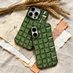 May include: Two green phone cases with a woven pattern are displayed. The cases have a glossy finish and are designed to fit specific phone models. The cases are on a surface with textured paper and wheat stalks.