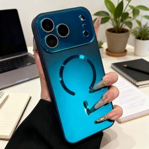 May include: A teal and navy blue phone case with a glossy finish. The case has a circular cutout and three camera cutouts. The case is held by a person with long, decorated nails. The case is designed to protect a smartphone.
