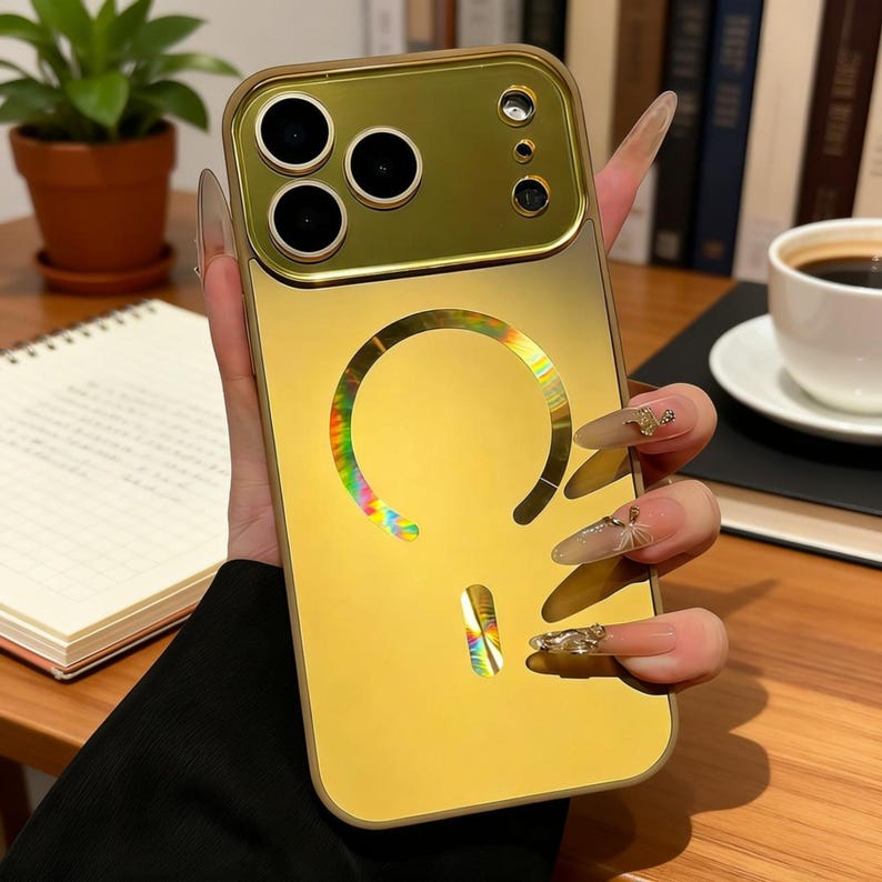 May include: A gold-colored phone case with a reflective, iridescent design. The case has a camera cutout and a circular design on the back. The phone case is held in a hand.