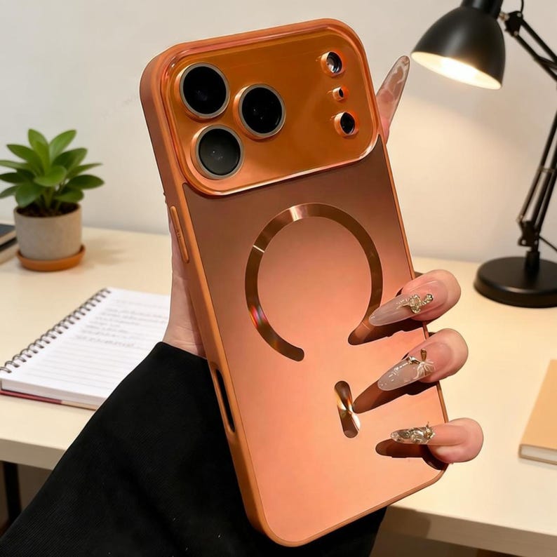 May include: A copper-colored phone case with a glossy finish. The case features a raised camera section and a circular design on the back. The case is designed to protect the phone and has a built-in ring holder.