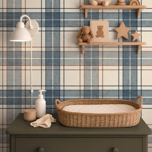 Puede incluir: Una escena de guarder&iacute;a con una c&oacute;moda verde, una cesta para cambiar pa&ntilde;ales de mimbre y una l&aacute;mpara de pared blanca. Estantes exhiben un oso de peluche, un conejito, juguetes de madera y una estrella. El fondo es un papel pintado a cuadros azul y blanco.