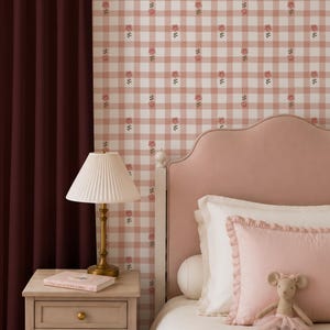 Op de afbeelding: Slaapkamerinterieur met een roze hoofdbord, een nachtkastje en een lamp. Het behang heeft een roze en wit geblokt patroon met bloemmotieven. Een knuffelmuis in een tutu ligt op het bed.