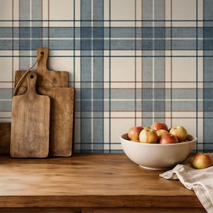 Puede incluir: Escena de cocina r&uacute;stica con encimera y armarios de madera. Tres tablas de cortar de madera se apoyan en un papel pintado a cuadros azul, blanco y marr&oacute;n. Un cuenco blanco contiene varias manzanas. Un pa&ntilde;o de lino est&aacute; sobre la encimera.
