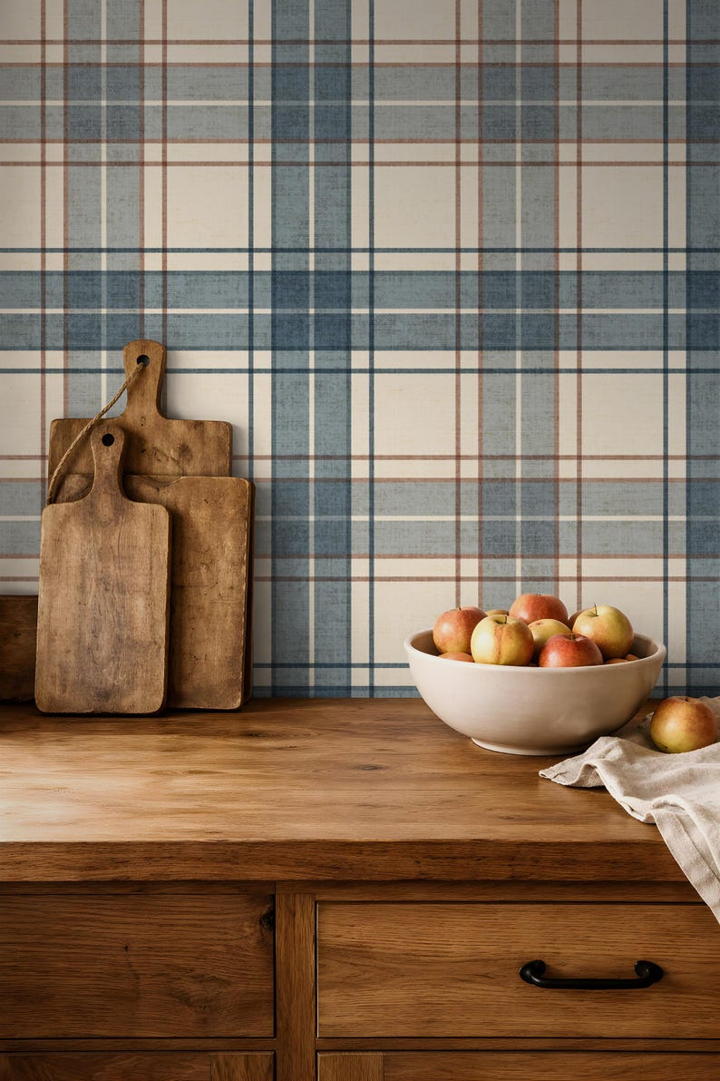 Puede incluir: Escena de cocina r&uacute;stica con encimera y armarios de madera. Tres tablas de cortar de madera se apoyan en un papel pintado a cuadros azul, blanco y marr&oacute;n. Un cuenco blanco contiene varias manzanas. Un pa&ntilde;o de lino est&aacute; sobre la encimera.