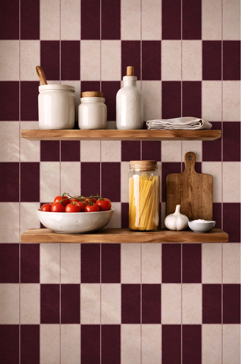 May include: Two horizontal wooden shelves mounted against a wall with a checkered pattern of dark maroon and off-white rectangular tiles. The shelves hold ceramic jars, a glass jar of pasta, a bowl of red tomatoes, a garlic bulb, and a board.
