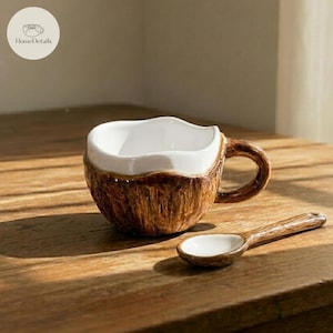 May include: A ceramic coffee cup and spoon set. The cup is designed to resemble a coconut, with a brown textured exterior and a white interior. A matching spoon rests beside the cup. The HomeDetails logo is in the upper left corner.