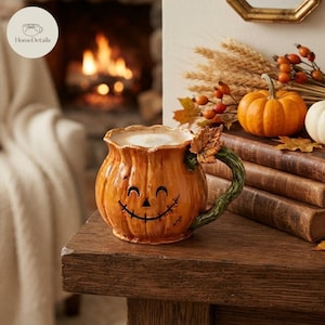 Può includere: Una tazza in ceramica a forma di zucca con finitura arancione lucida, caratterizzata da un volto di jack-o'-lantern intagliato con un sorriso cucito. Il manico è disegnato come un viticcio verde con una piccola foglia vicino al bordo.
