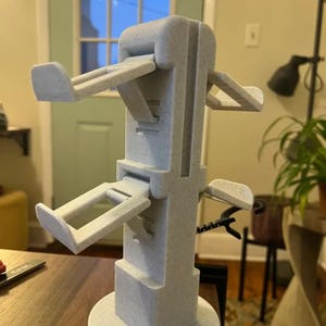 Puede incluir: Un soporte gris claro, impreso en 3D, con múltiples brazos angulados, diseñado para sostener objetos. El soporte tiene una base circular y una estructura central alta y rectangular. Los brazos se extienden hacia afuera a varios niveles.