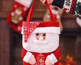 Pode incluir: Uma sacola de presente em tricô vermelho com um design de Papai Noel, barba de pelúcia branca, gorro com estampa vermelha e branca e duas alças vermelhas. A sacola inclui um pequeno botão bege na frente e punhos de pelúcia branca.