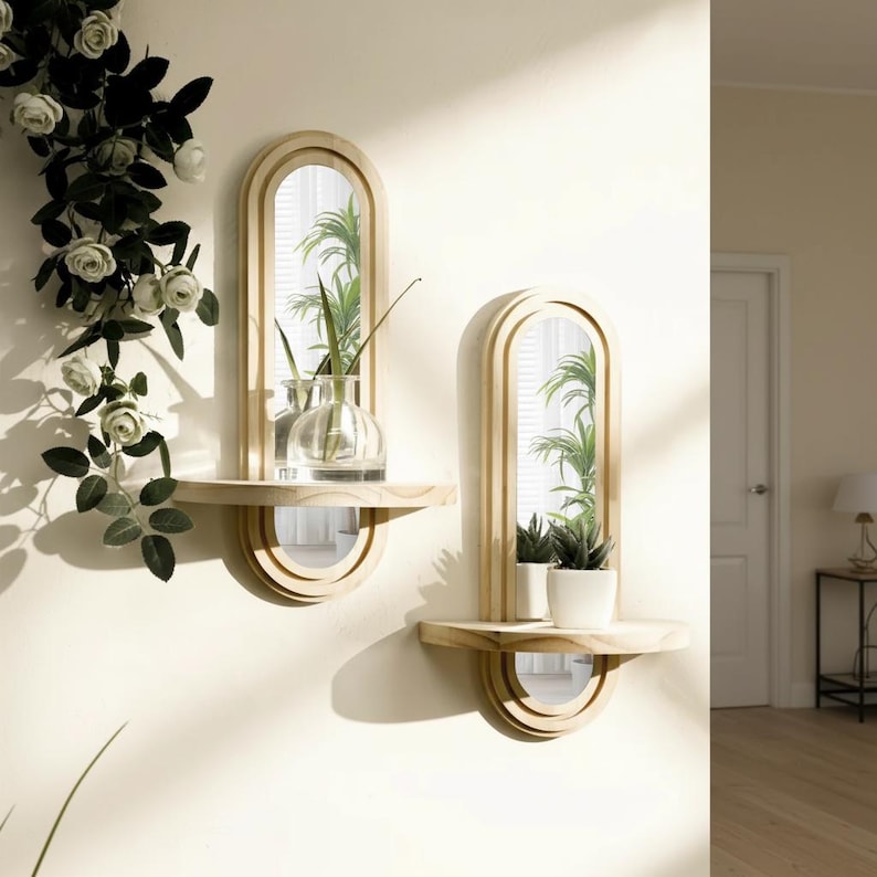 May include: Two wooden wall mirrors with arched frames and attached shelves. Each mirror has a small, round shelf below the mirror. One shelf holds a clear vase with greenery, the other holds potted plants. The mirrors are mounted on a light-colored wall.