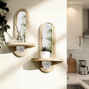 May include: Two wooden wall shelves with arched mirrors. Each shelf has a small shelf and a semi-circular mirror below the main mirror. One shelf holds a clear vase with a plant stem, the other a potted succulent.