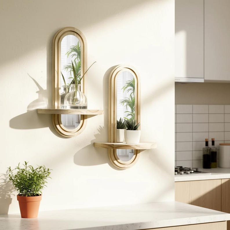 May include: Two wooden wall mirrors with shelves, each featuring an arched mirror design. One shelf holds a glass vase with greenery, the other holds potted plants. The mirrors are mounted on a white wall, with a terracotta pot of greenery in the foreground.