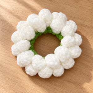 May include: A circular hair scrunchie made of white yarn crocheted into a series of small, rounded, puffy clusters. The inner ring of the scrunchie is constructed from bright green yarn, providing a contrast to the white outer texture.