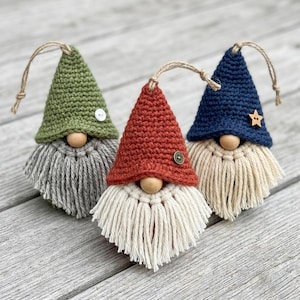 May include: Three handmade gnome ornaments with crochet hats in green, red, and blue. Each gnome has a wooden bead nose and a yarn beard. The green gnome has a white button, the red gnome has a brown button, and the blue gnome has a wooden star.