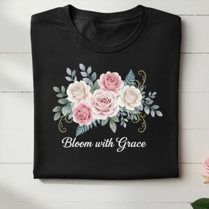 May include: Black t-shirt with a floral design. The design includes pink and white roses, green leaves, and the text "Bloom with Grace". The t-shirt is neatly folded.