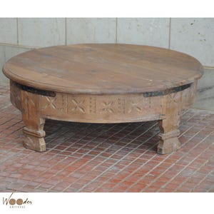 May include: A round, wooden coffee table with a distressed finish. The table features carved floral designs around the apron and rests on four sturdy, square legs. The table is approximately 30 inches in diameter.