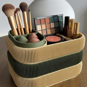 May include: A three-tiered makeup organiser in beige, green, and black. The top tier holds makeup brushes, sponges, and a small tray. The middle tier is green, and the bottom tier is black. The organiser is filled with makeup products, including eyeshadow palettes, blush, and foundation.
