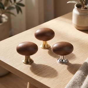 May include: Three oval-shaped cabinet knobs featuring smooth, dark brown wooden tops. Each knob is mounted on a metallic base, with two knobs displaying a brushed brass finish and one knob featuring a polished silver-tone chrome finish.