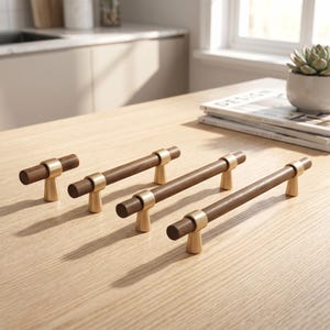 Könnte beinhalten: Ein Set aus vier Schrankgriffen mit zylindrischen, dunkelbraunen Holzstangen und gebürsteten goldfarbenen Metallhalterungen. Das Set besteht aus einem kleinen knopfförmigen Griff und drei längeren Stangengriffen mit je zwei Metallstützen.