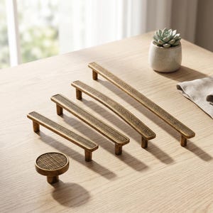 May include: A collection of antique brass cabinet hardware including one round knob and three linear drawer pulls of varying lengths. Each piece features a textured, cross-hatched grid pattern on the top surface and a smooth, metallic finish.
