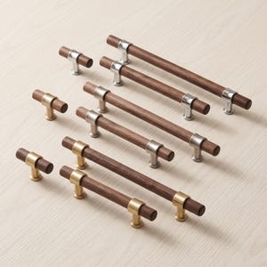 Puede incluir: Una colección de tiradores para armarios con barras cilíndricas de madera marrón oscuro combinadas con soportes de montaje de metal en tono plateado pulido o dorado cepillado. El juego incluye varias longitudes y pomos.