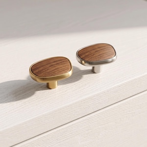 May include: Two cabinet knobs with irregular, rounded shapes. One knob features a brushed gold metal base with a dark wood grain inlay, while the other has a brushed silver metal base with a matching dark wood grain inlay on the top surface.