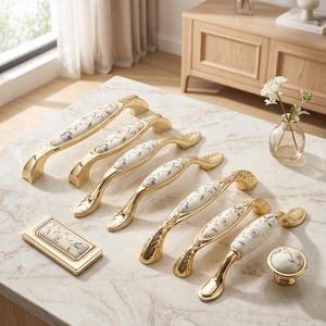 May include: A collection of gold-toned cabinet hardware, including handles and a knob. The handles feature a white ceramic center with a floral design in purple and green. The hardware is arranged on a marble surface.