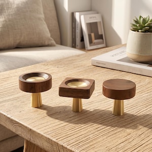 May include: Three cabinet knobs featuring dark brown wood tops and conical brass bases. Two knobs have circular wooden tops with recessed brass centers, while the third knob has a solid circular wooden top. Each piece stands on a tapered brass post.