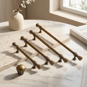 May include: A collection of antique brass hardware including three elongated cabinet pulls and one matching round knob. Each piece features a fluted, ribbed design at the ends and center, showcasing a metallic finish with subtle dark highlights.