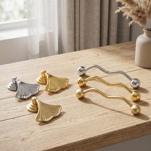 Peut inclure: Une collection de quincaillerie d'ameublement en métal comprenant trois poignées en forme d'éventail aux finitions argent et or poli, ainsi que trois poignées barres ondulées en argent poli, or poli et or mat avec des extrémités sphériques.