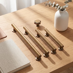 May include: A collection of antique brass hardware including three long, straight cabinet pulls with hexagonal mounting bases and one matching hexagonal cabinet knob. The metal hardware features a brushed, weathered finish with visible texture.
